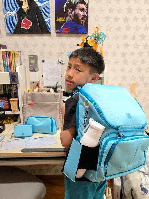 Child wearing a blue backpack with a desk and posters in the background