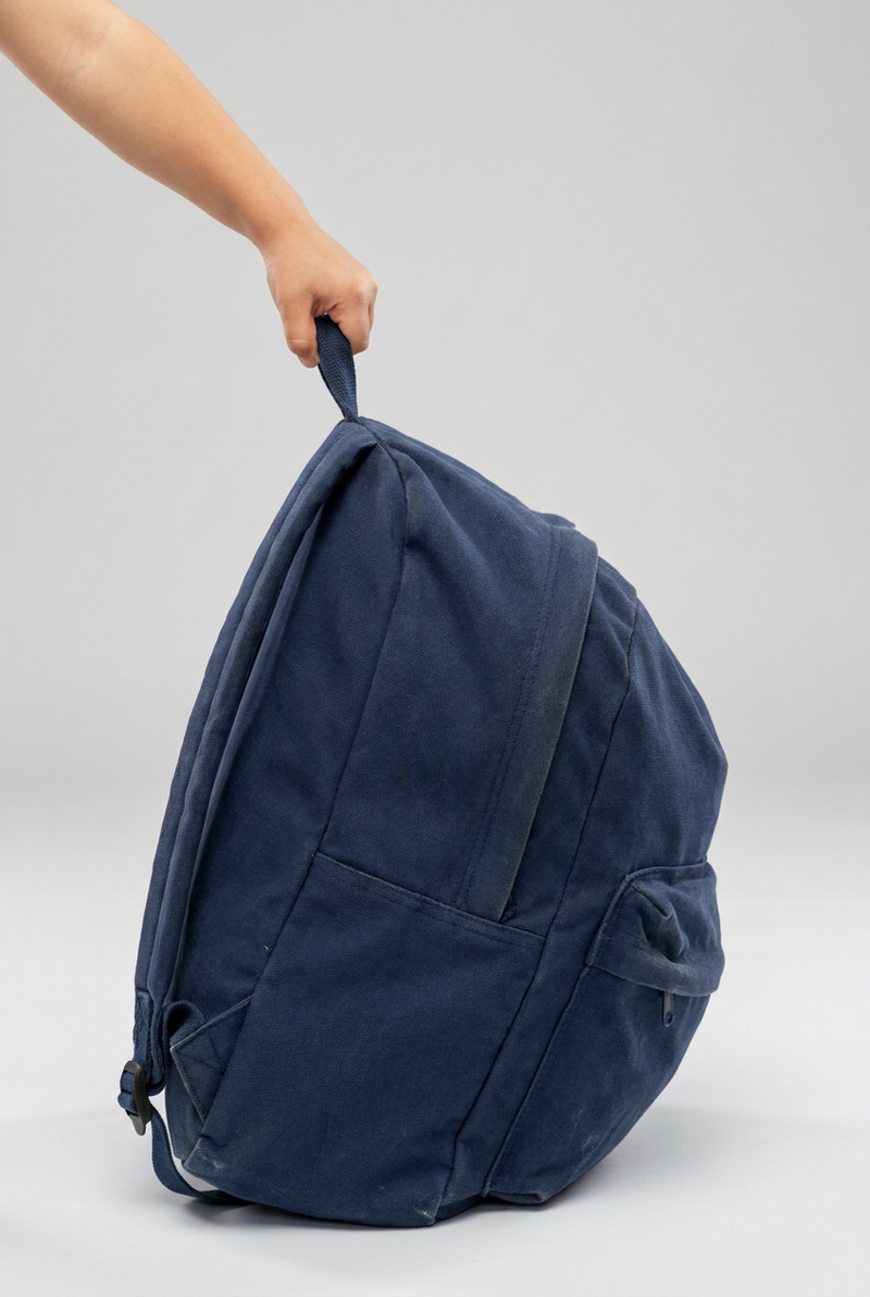Overstuffed backpack in navy blue. A child's hand is holding the backpack.