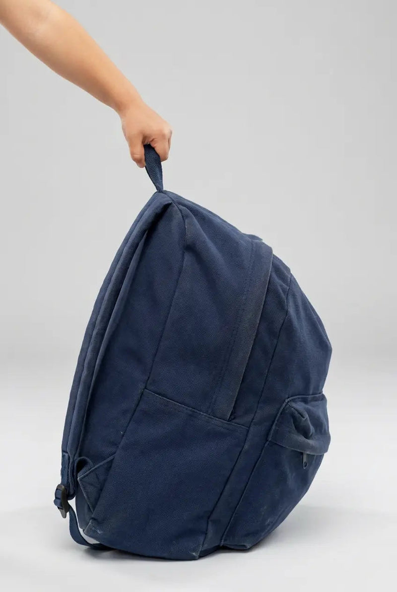 Overstuffed backpack in navy blue. A child's hand is holding the backpack.