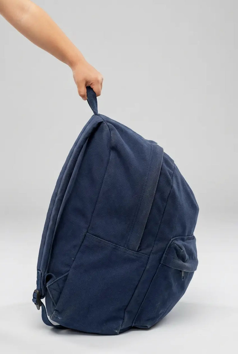 Overstuffed backpack in navy blue. A child's hand is holding the backpack.
