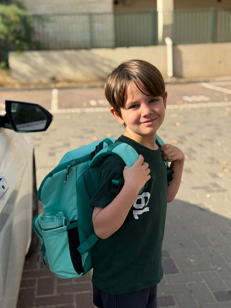 Child with a teal backpack standing next to a car on a street.