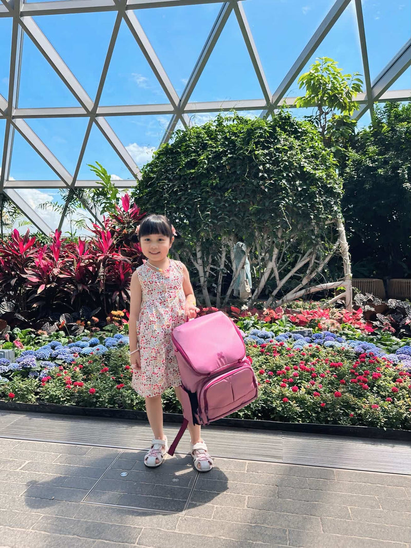 Child holding a pink suitcase in front of a floral display