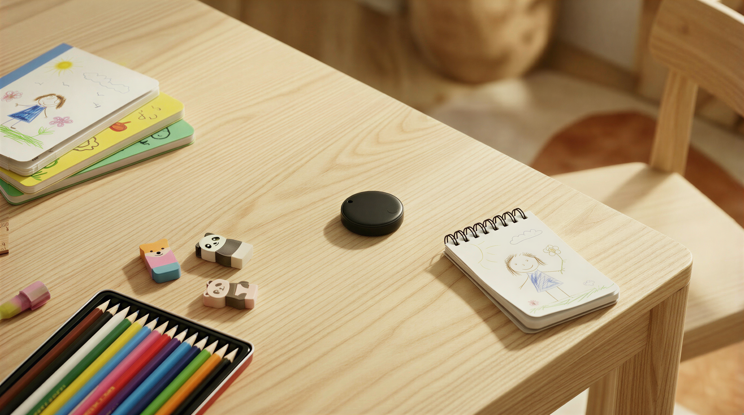 Children's stationery items on a wooden table with a bluetooth tracker in the 