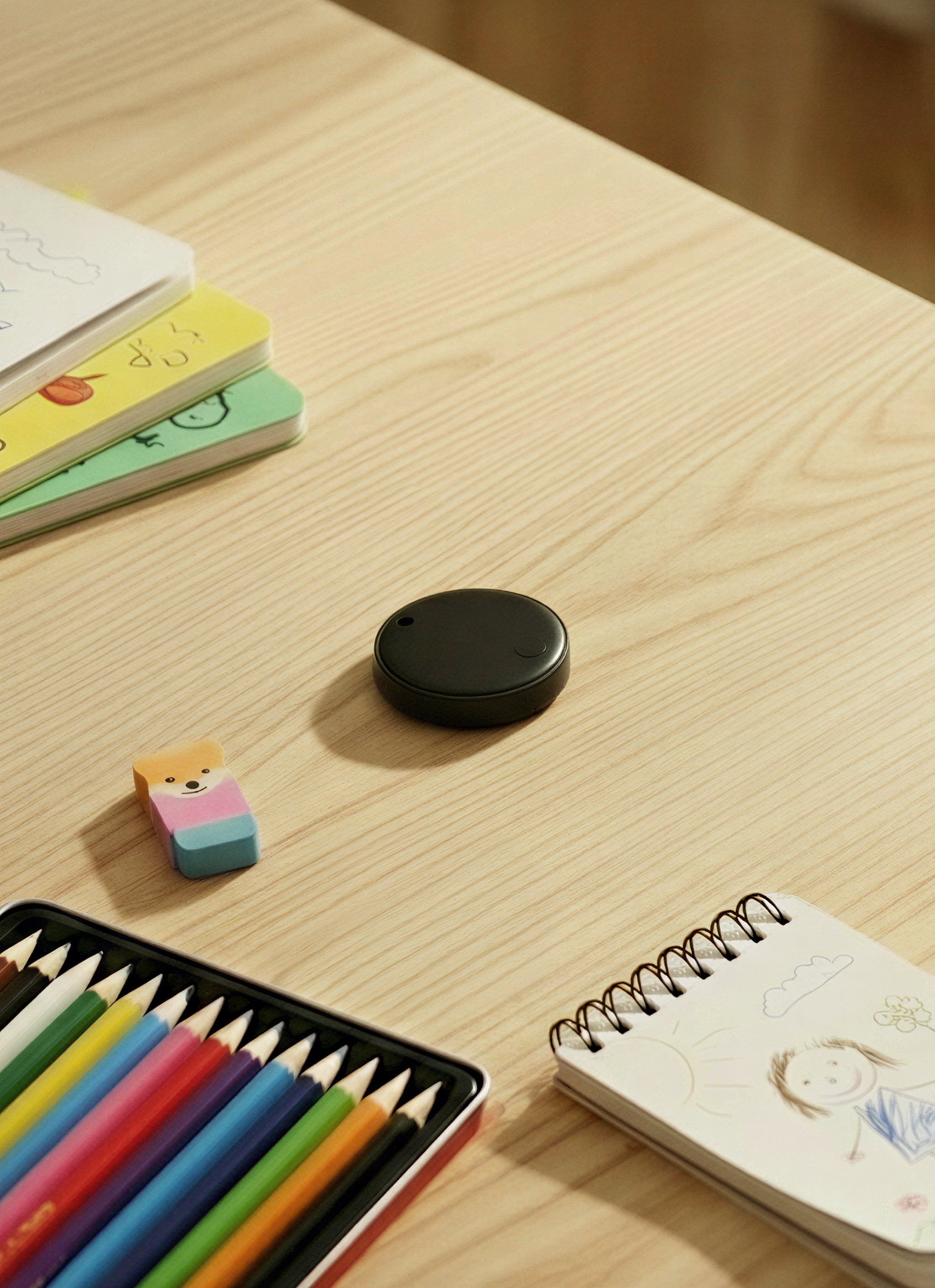 Children's stationery items on a wooden table with a bluetooth tracker in the center