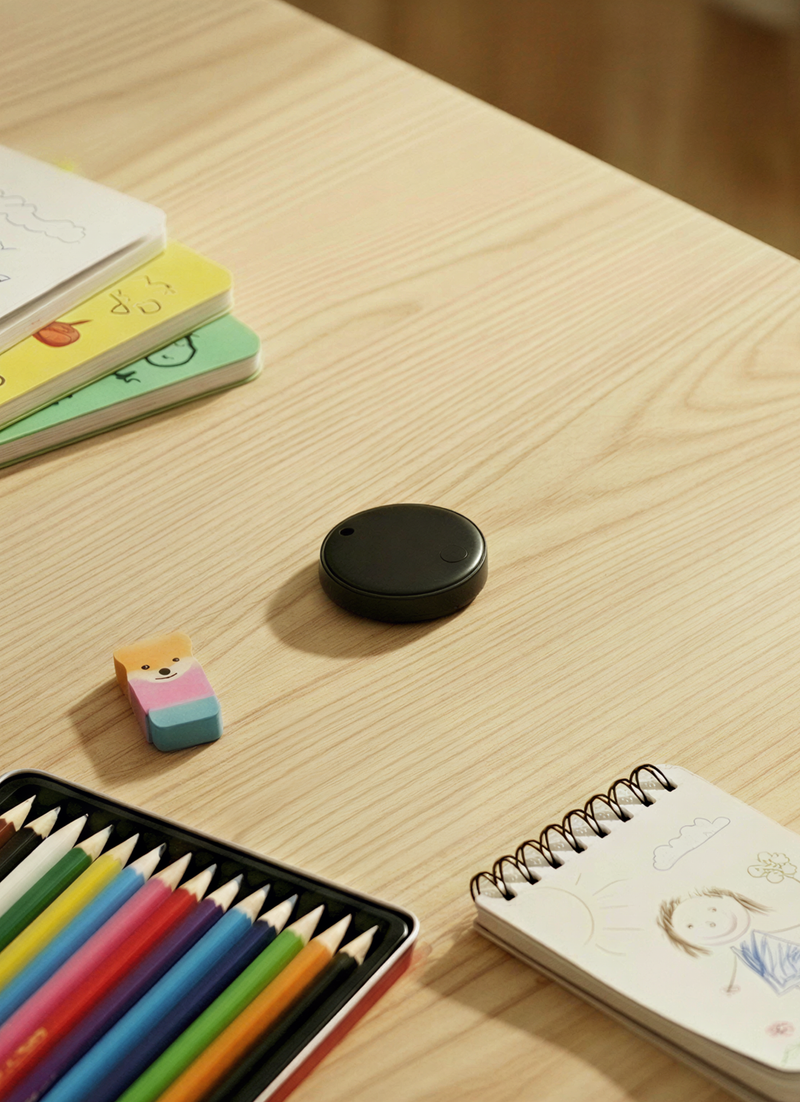 Children's stationery items on a wooden table with a bluetooth tracker in the centre of the shot.